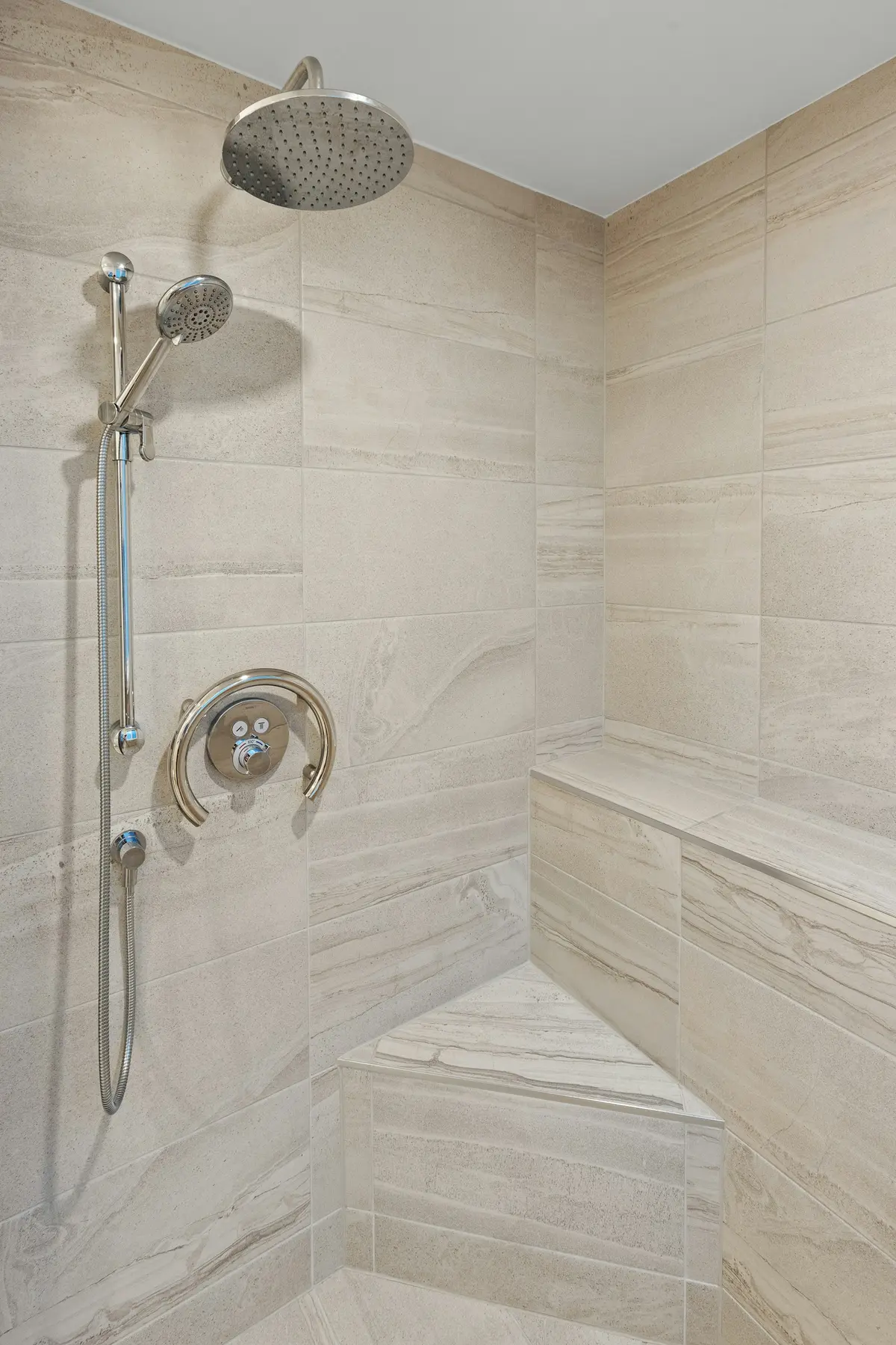 Shower wall with stone-look tile, a bench and a handheld shower