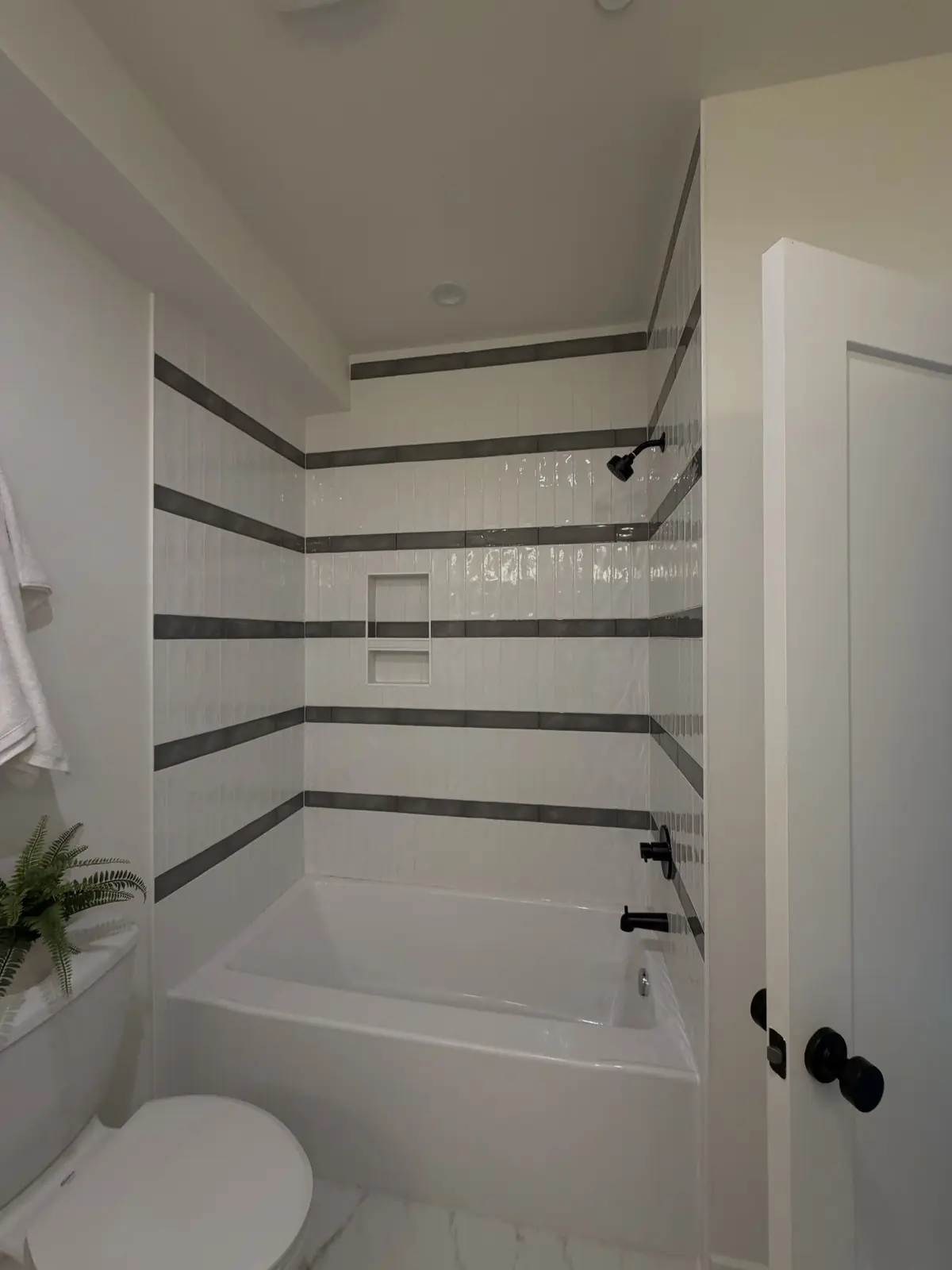 Tub surround with white vertical tile and grey accent bands aligned across all three walls, with a recessed niche